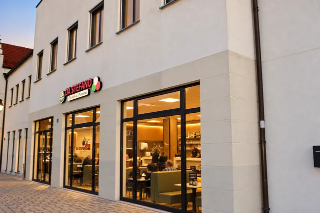 Da Stefano an der Gebäudeecke mit großen Fensterfronten am Abend
